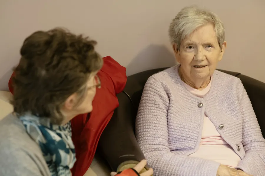 En äldre kvinna och hennes vuxna dotter sitter bredvid varandra och pratar.